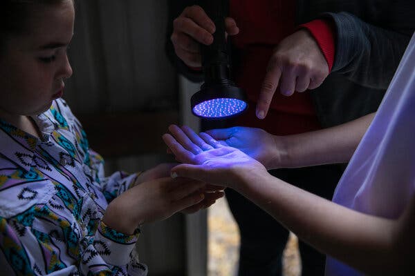 Dr. Nolting holds a blacklight over the hands of children and points out germs illuminated by the light.